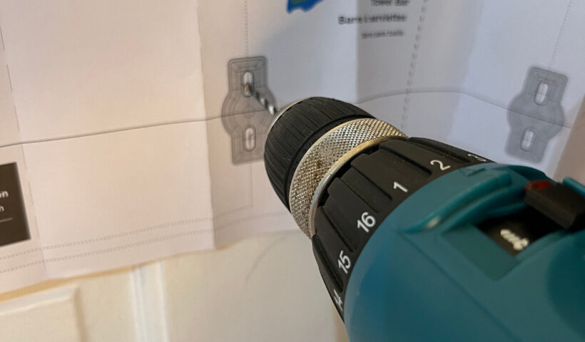 Teal Makita drill with bit in place drilling holes using a paper template for the towel bar DIY small space storage solutions