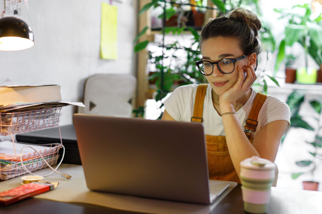 Woman in glasses with hair up in front of a computer, writing, green plants behind her, 1-3-5 Rule