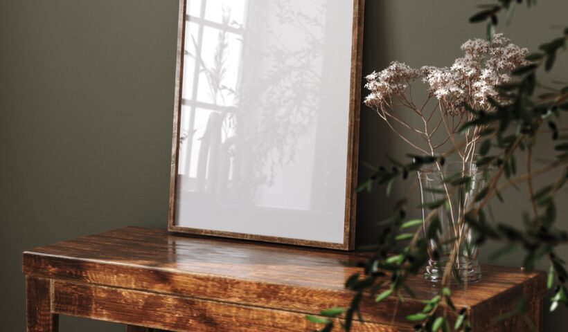 vintage table, empty picture frame, botanicals and green plant against a dark green wall for underconsumption core design trend