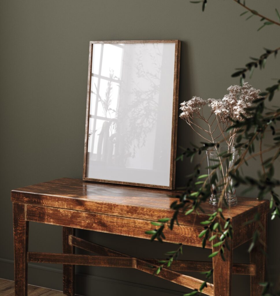 vintage table, empty picture frame, botanicals and green plant against a dark green wall for underconsumption core design trend