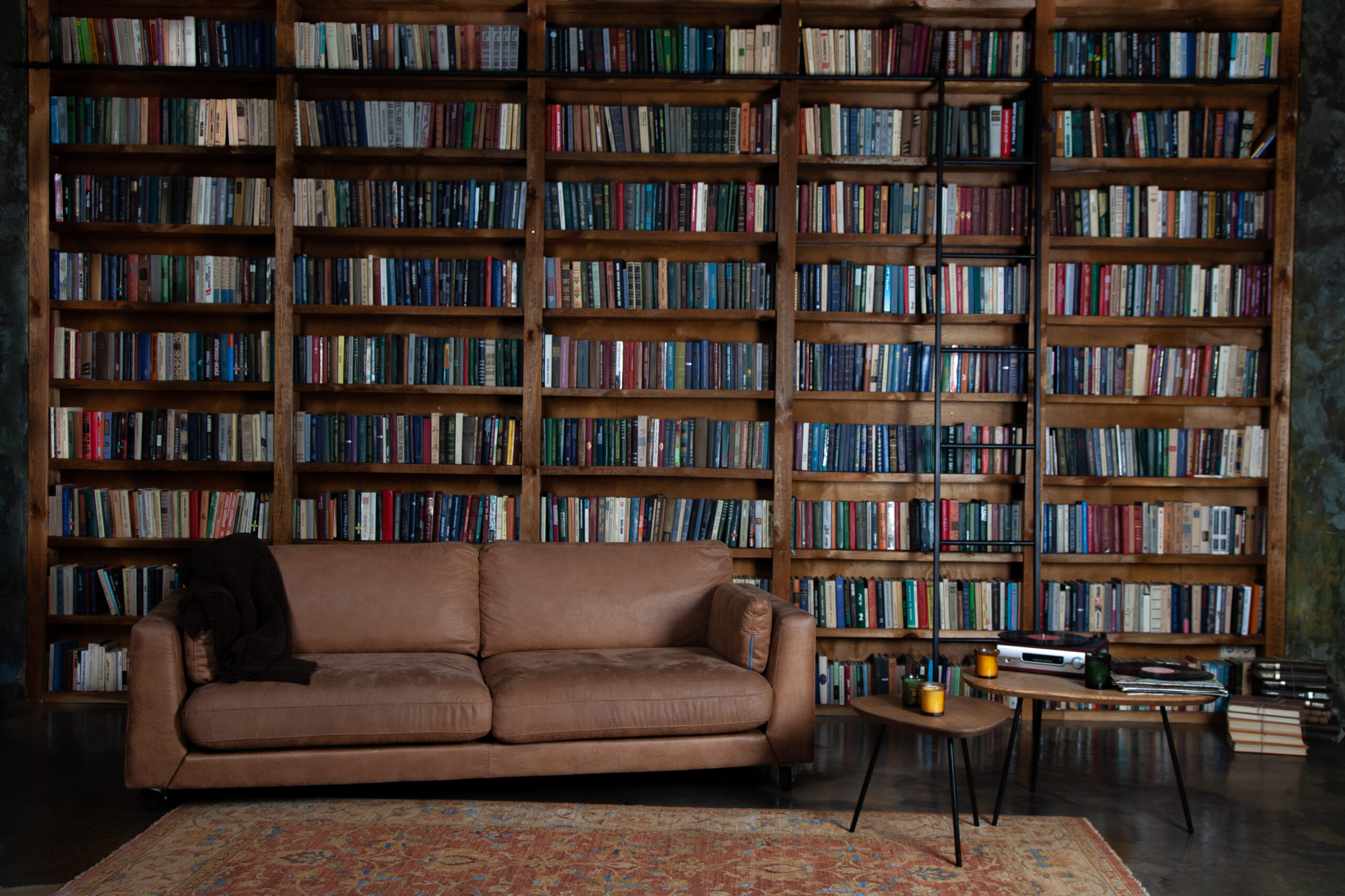 Dark Academia Fall Aesthetic Dark brown leather couch with blanket over it against a wall of dark brown bookshelves, next to small tables with candles and media players, Shutterstock, Real_Life_Photo