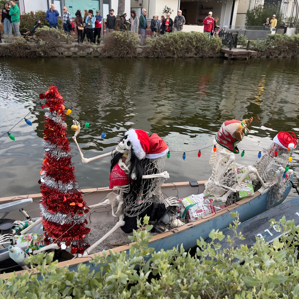 Skeletons and red Christmas tree in row boat Venice Canal Boat Parade Christmas Decorations Holiday Decorations California Celebration